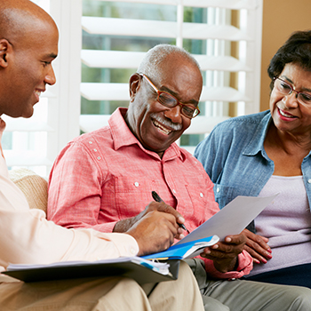 A financial advisor sitting on a sofa and talking to a senior couple in their home.