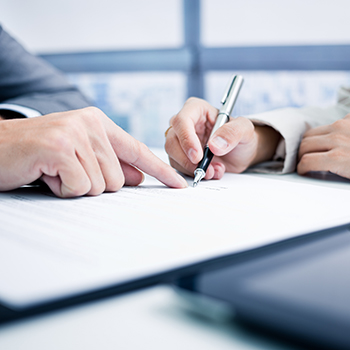 A close-up view of a person's hands signing a contract on a clipboard.