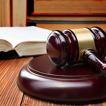 A wooden judge's gavel resting on a law book on a desk, with stacked law books out of focus in the background.